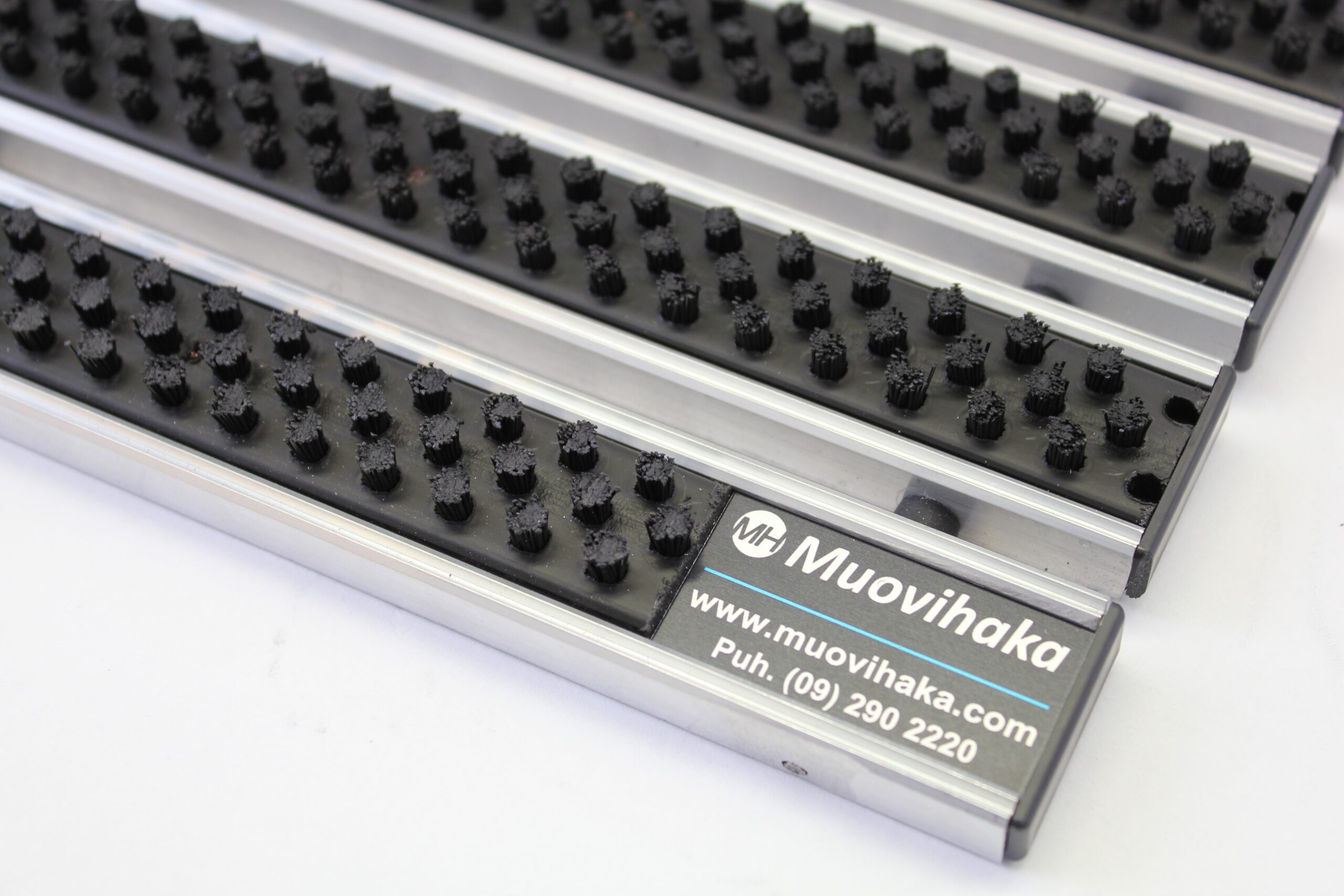 Close-up of Venture Brush entrance grid with black cleaning brushes, aluminium profiles and Muovihaka product label